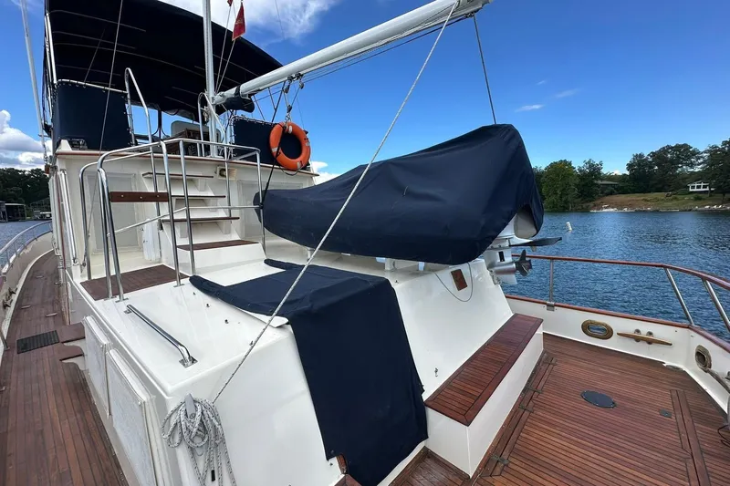 30 West Yacht Photos Pics 1991 Grand Banks 49 Classic yacht deck with covered equipment, docked by a scenic shoreline.
