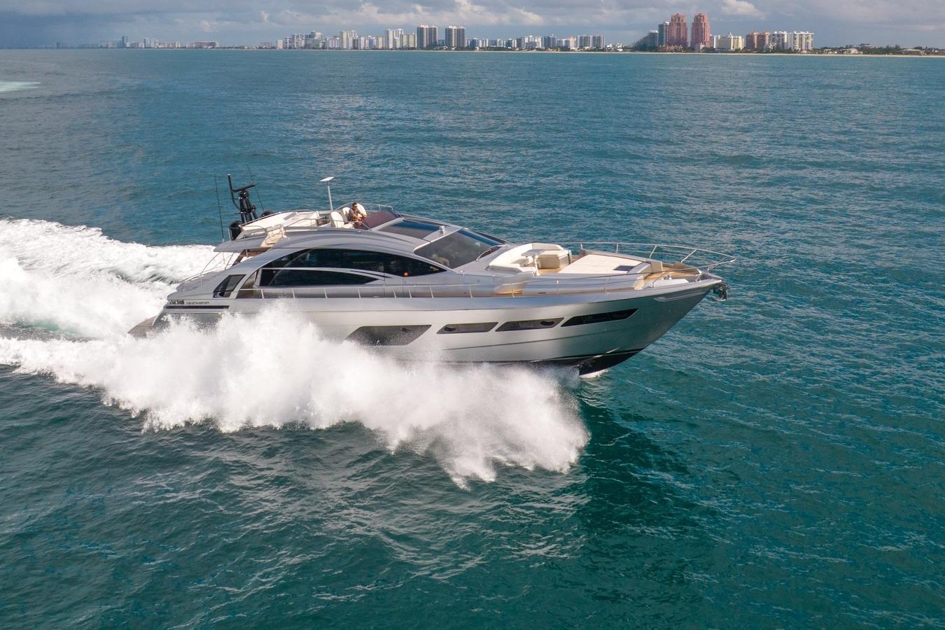 2020 Pershing 8X yacht cruising on open water with city skyline backdrop.