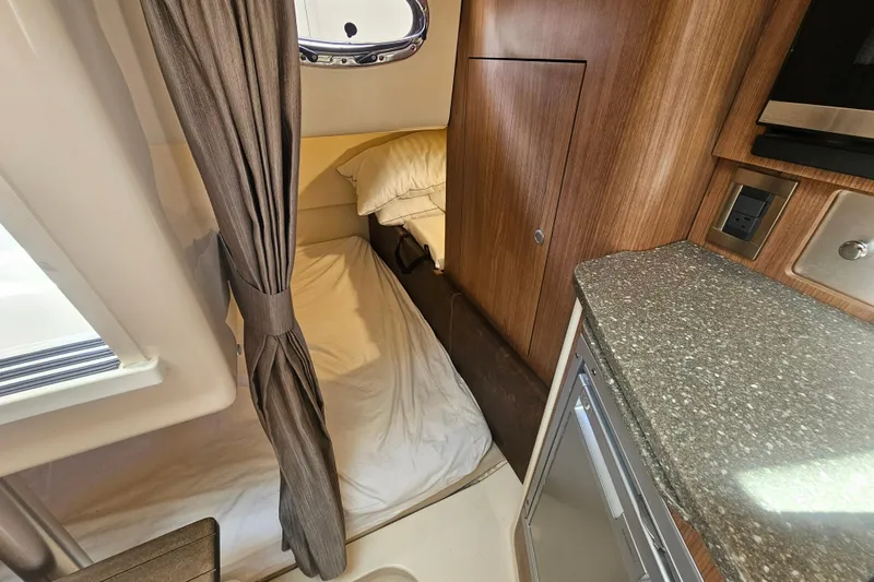 Day For It Yacht Photos Pics 2018 Boston Whaler 315 Conquest cabin interior with bed, curtain, and kitchenette.