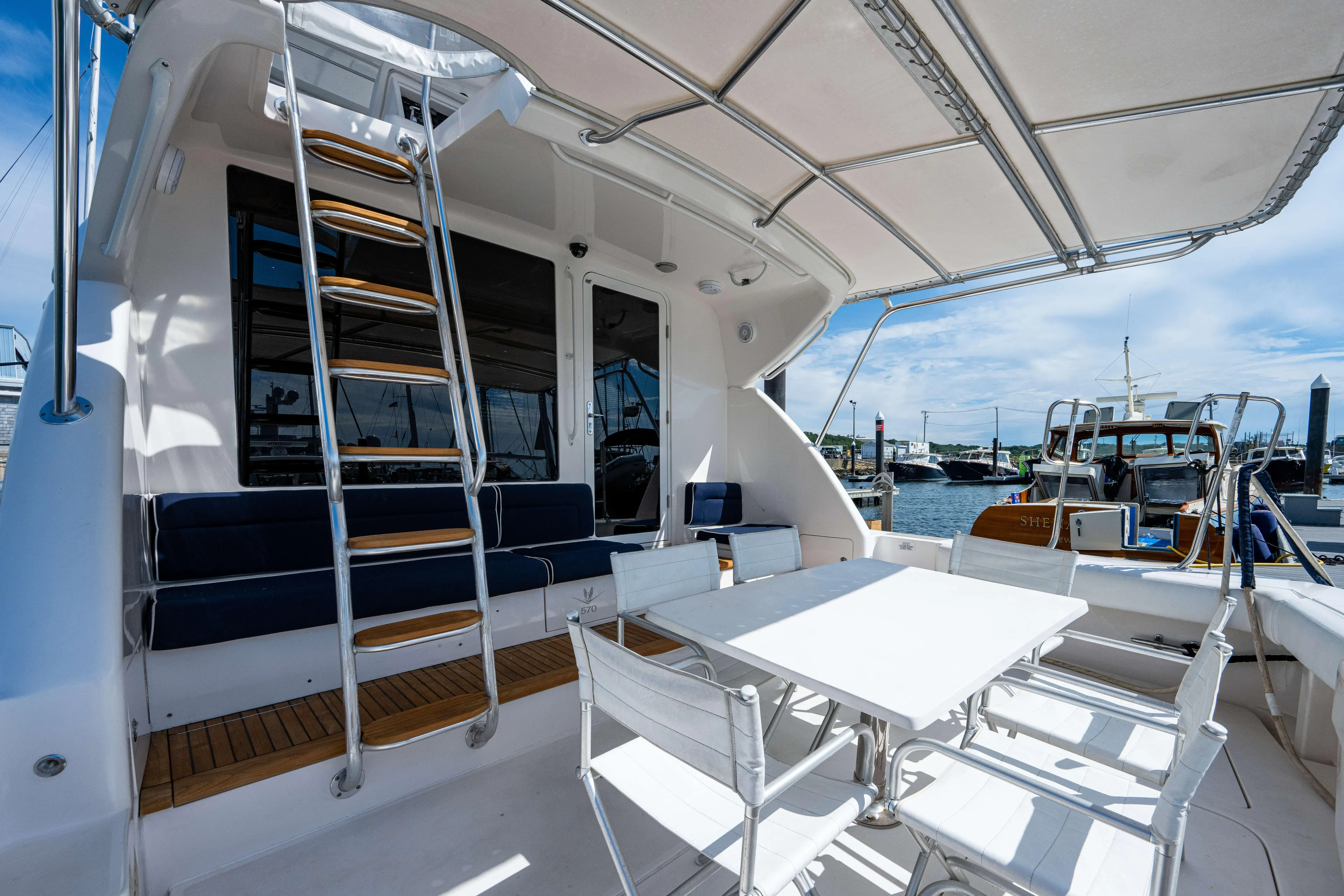 Nine Yacht Photos Pics 2008 Bertram 570 yacht deck with seating, table, and ladder, docked at marina.