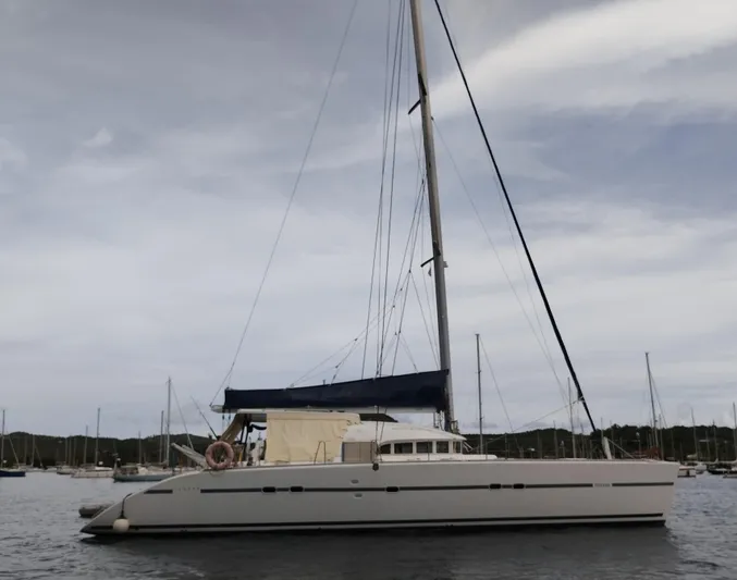  Yacht Photos Pics 2004 Lagoon 570 catamaran anchored in a serene harbor under a cloudy sky.