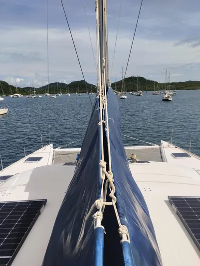  Yacht Photos Pics 2004 Lagoon 570 catamaran with blue sail, anchored in scenic bay with distant hills.