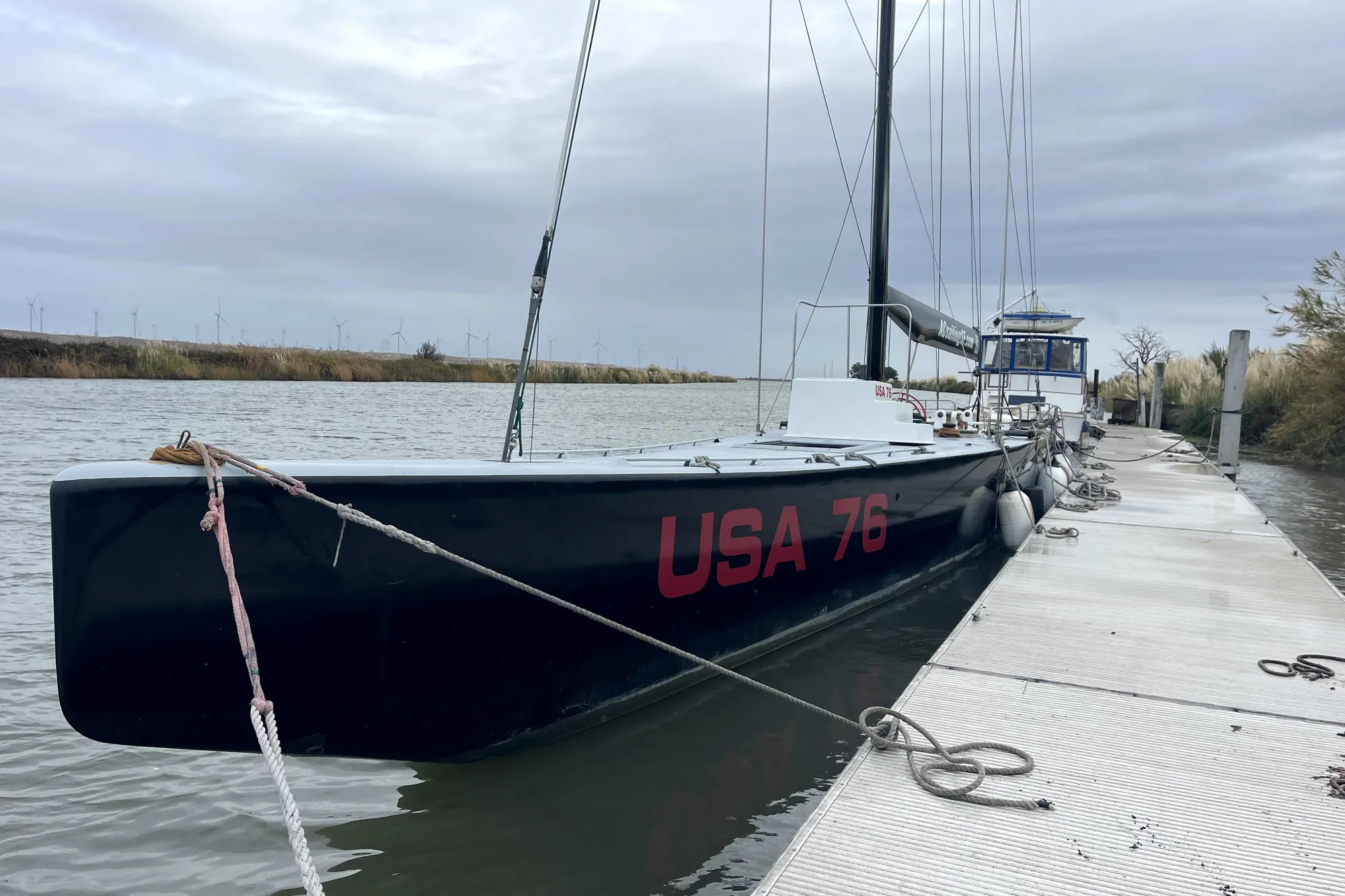 Sleek 2002 Custom International Americas Cup Class yacht "USA 76" docked by a riverbank.