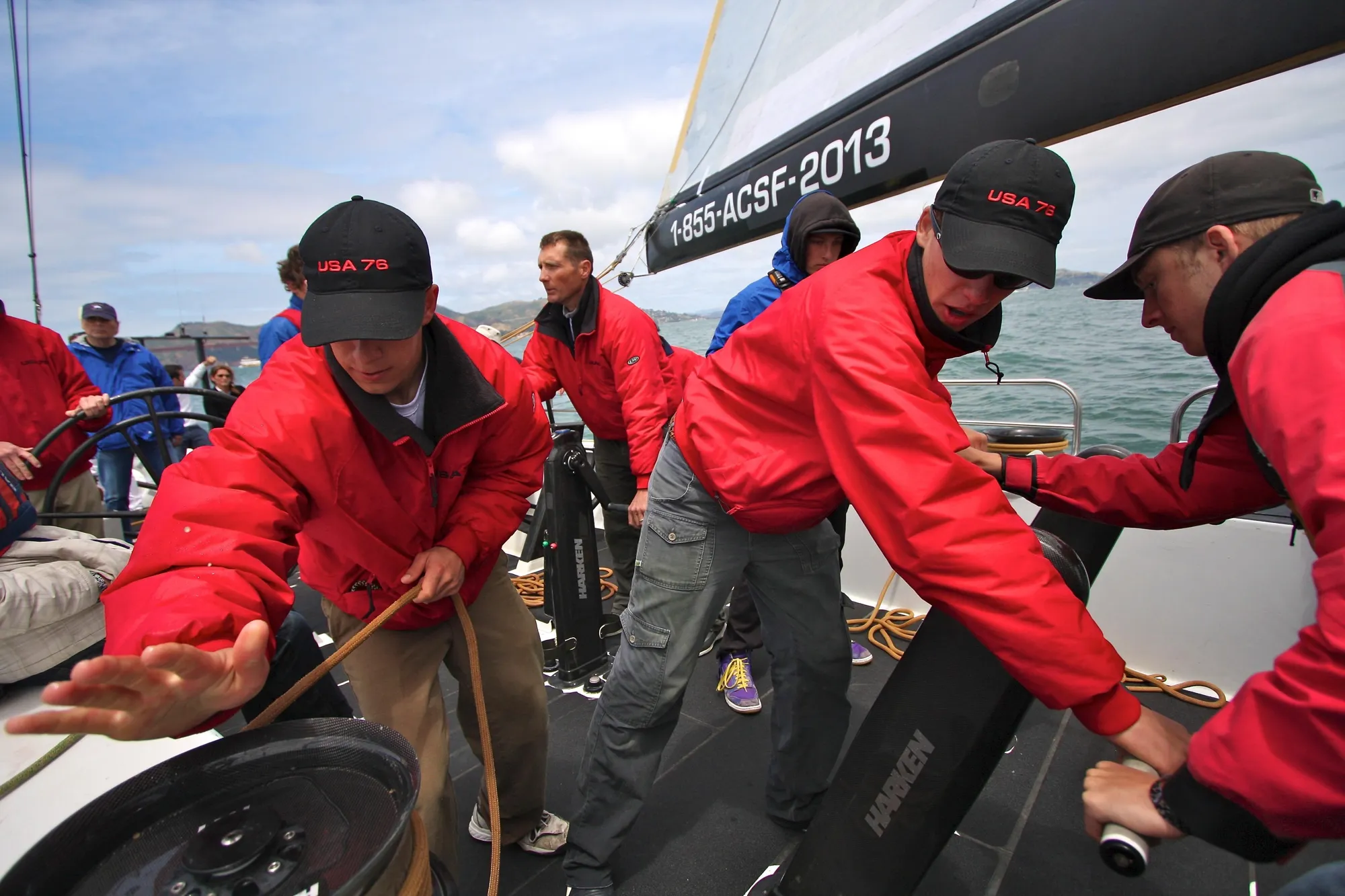 Crew members in red jackets operating winches on a 2002 International Americas Cup Class yacht.