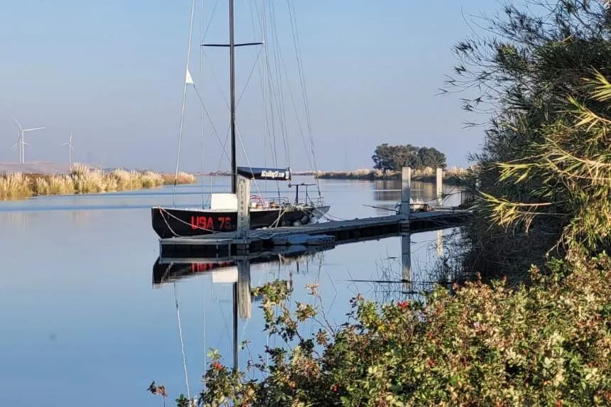 Sailboat "USA 76" docked on calm water, surrounded by nature, 2002 International Americas Cup Class.
