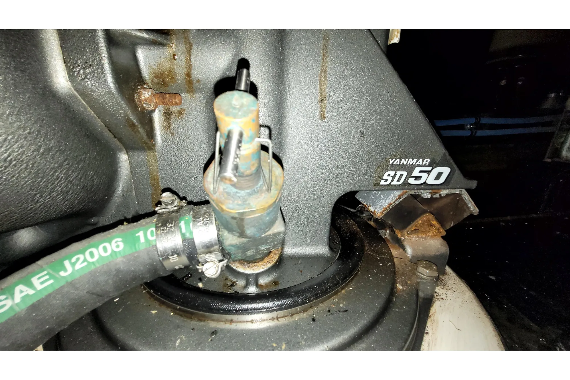 Close-up of Yanmar SD50 engine component with hose, showing rust and wear.
