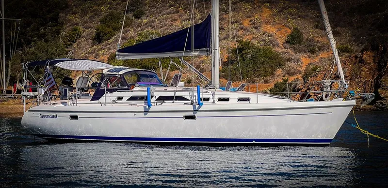 Moondust Yacht Photos Pics 1997 Catalina 380 sailboat anchored near a rocky shoreline with lush greenery.