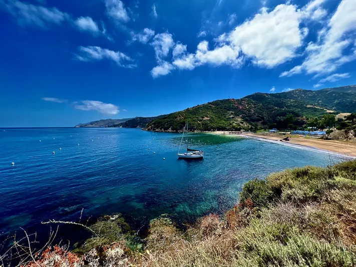 Moondust Yacht Photos Pics Sailboat anchored in a serene bay with lush hills and clear blue skies.