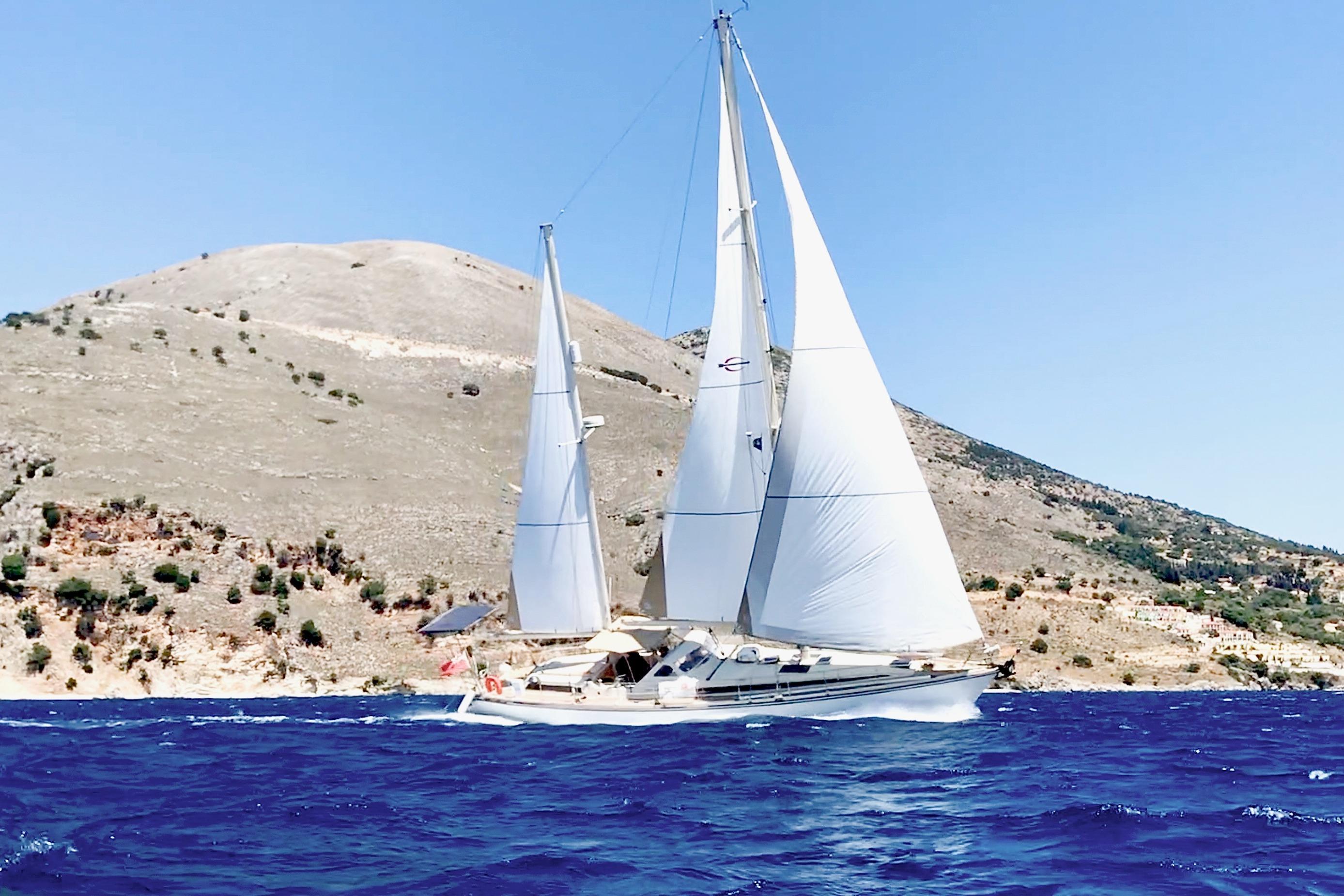 Sailing yacht Amel Super Maramu 1997 on blue sea with mountainous backdrop.