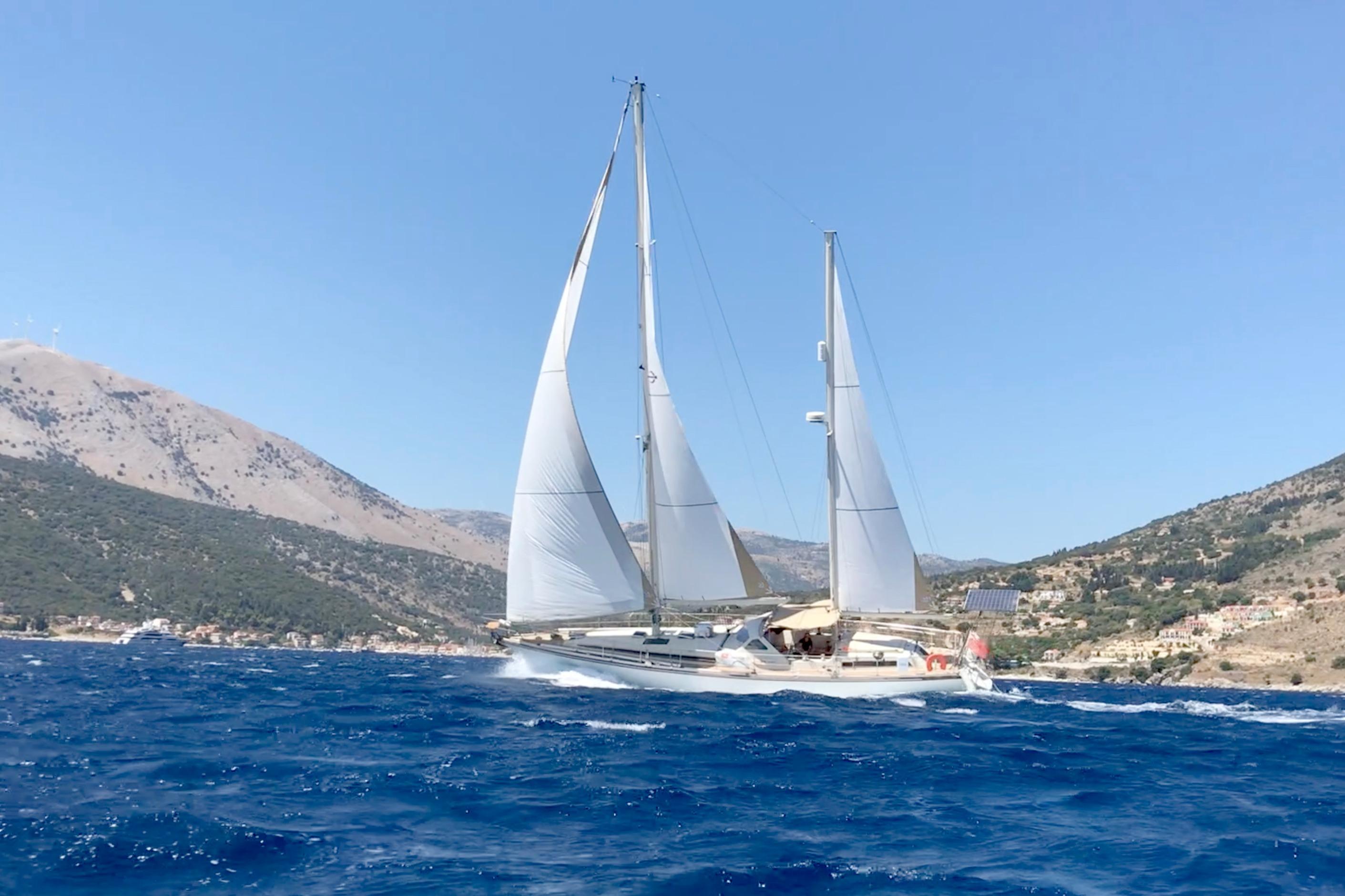 Sailing yacht Amel Super Maramu 1997 on blue sea with mountainous coastline.