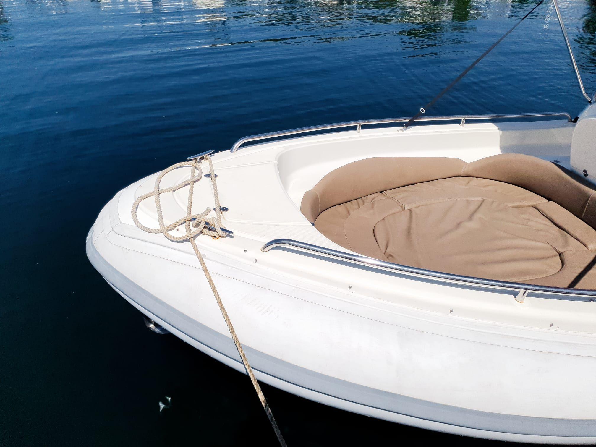 Bow of a white boat with beige seating, docked on calm water.