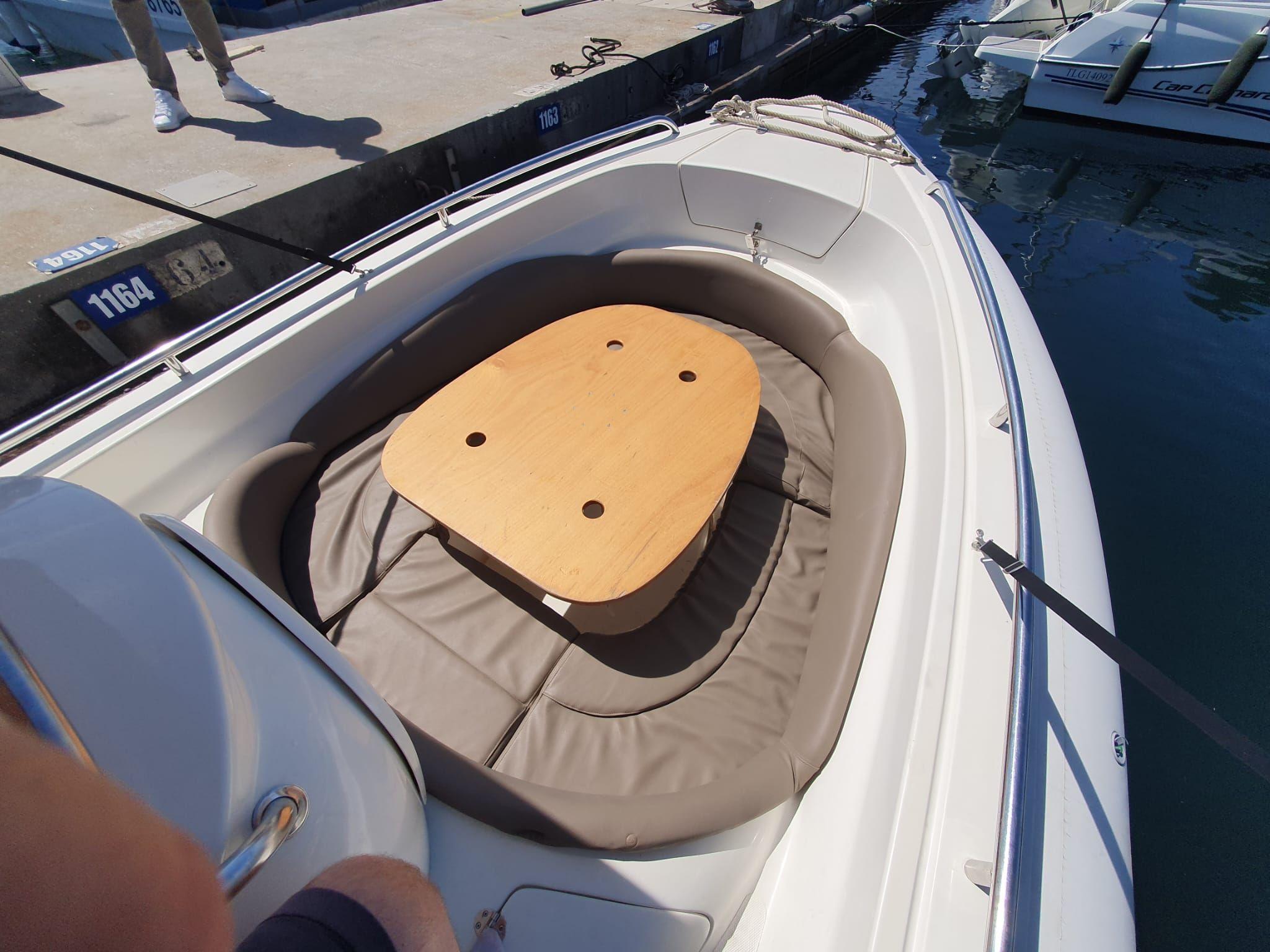 Small boat with cushioned seating and wooden table, docked at marina.