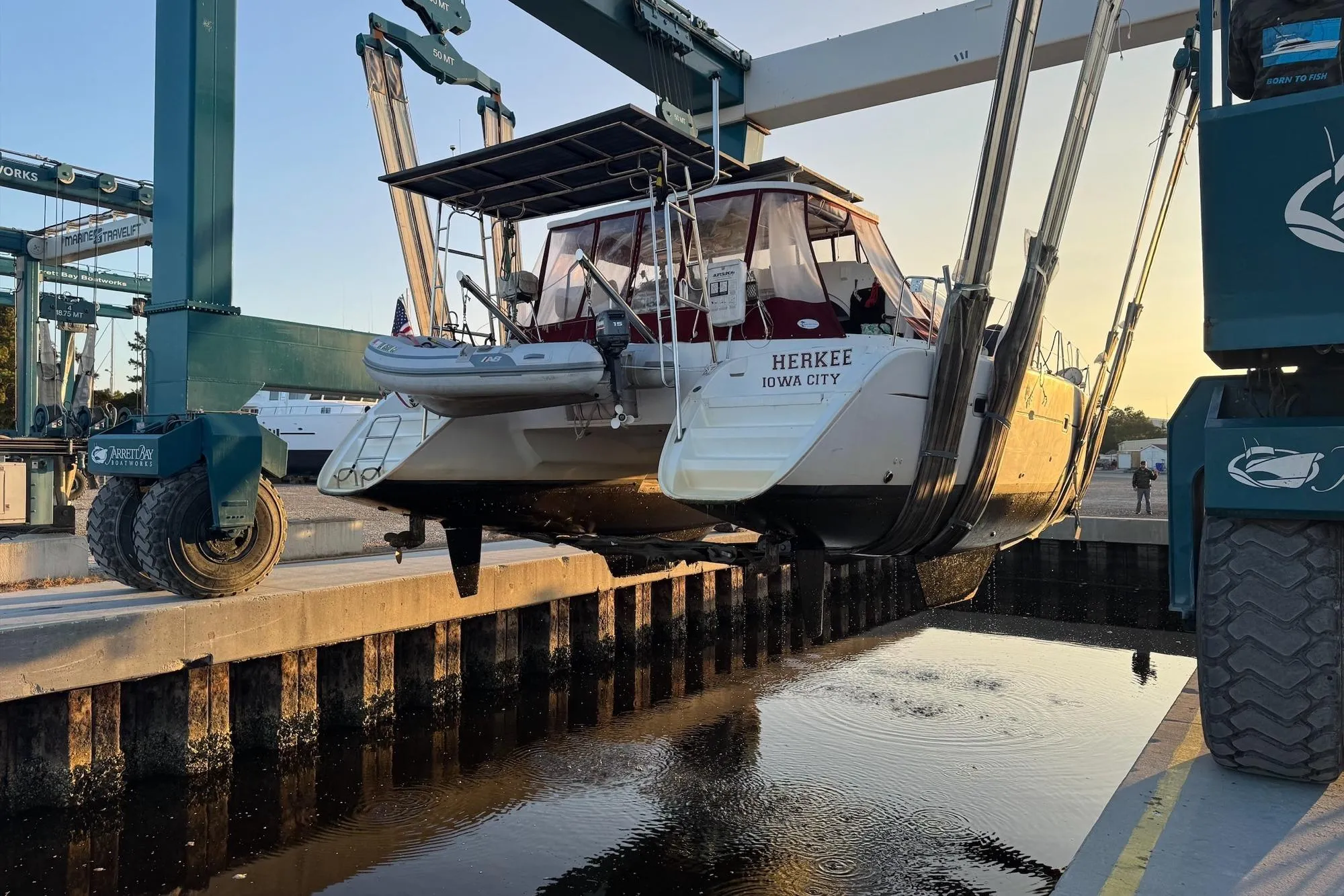 A 2004 Lagoon 380 catamaran being lifted by a boat hoist at a marina.