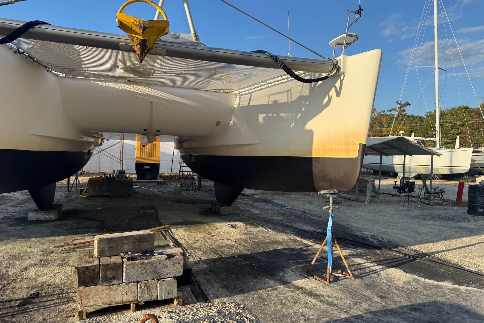 2004 Lagoon 380 catamaran on dry dock, undergoing maintenance with clear blue sky.