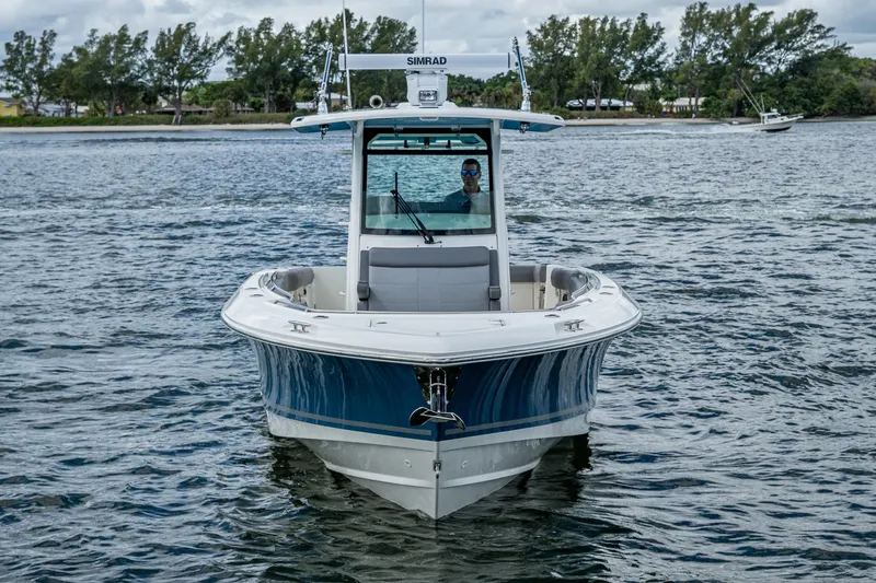  Yacht Photos Pics 2023 Boston Whaler 330 Outrage boat on water, front view, with trees in background.