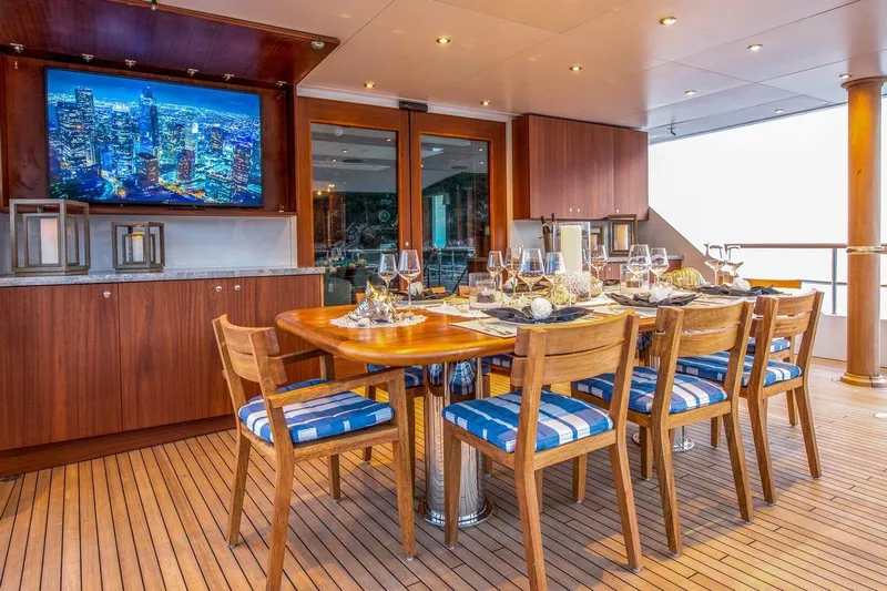  Yacht Photos Pics Luxurious yacht dining area with wooden table, blue cushioned chairs, and cityscape TV display.