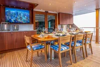 Luxurious yacht dining area with wooden table, blue cushioned chairs, and cityscape TV display.