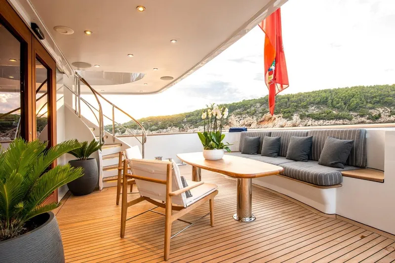  Yacht Photos Pics Luxurious yacht deck with seating, table, and plants, featuring a scenic coastal view.