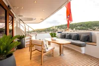 Luxurious yacht deck with seating, table, and plants, featuring a scenic coastal view.
