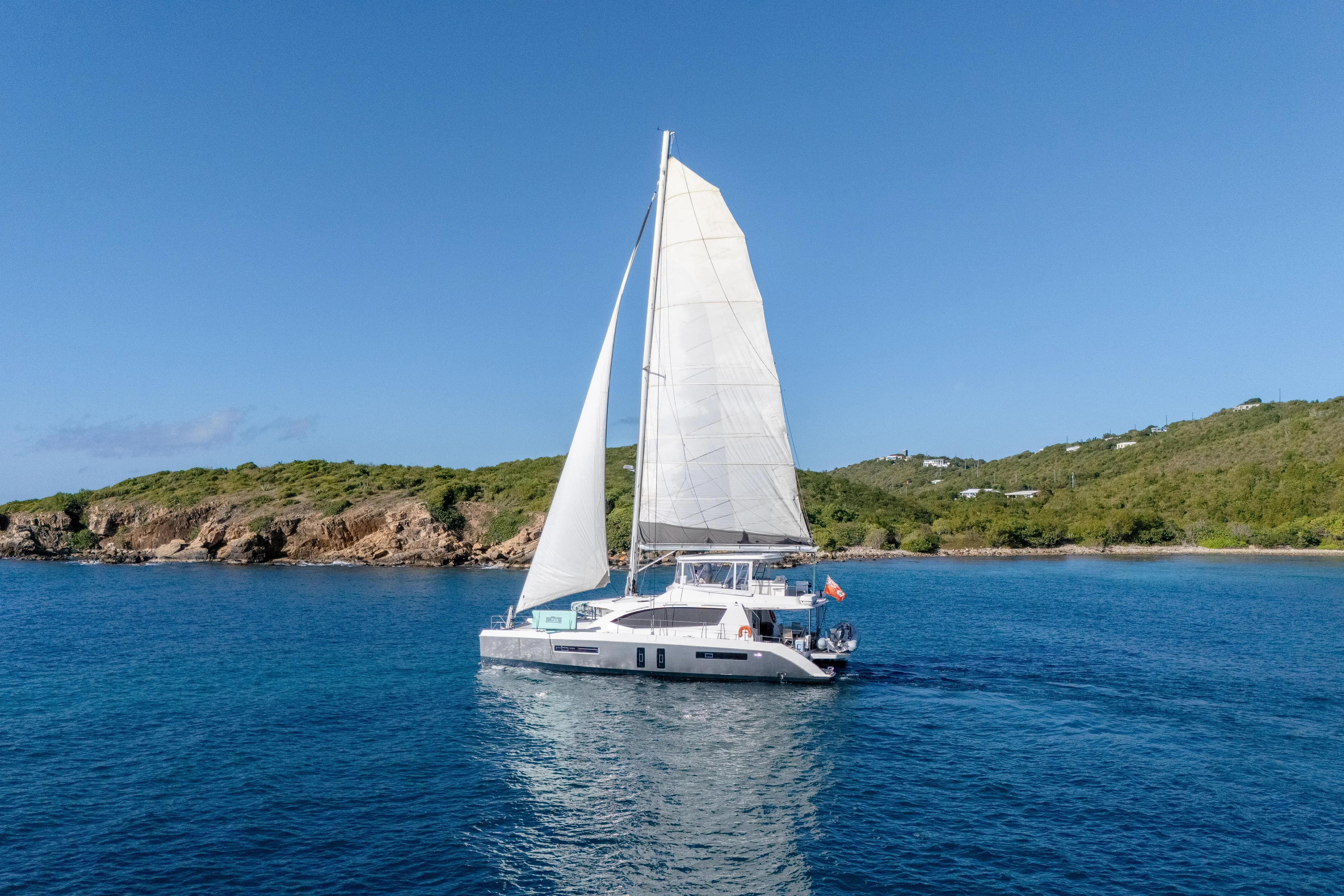 Sailing catamaran Leopard 58, 2014 model, cruising near a lush coastline under clear blue skies.