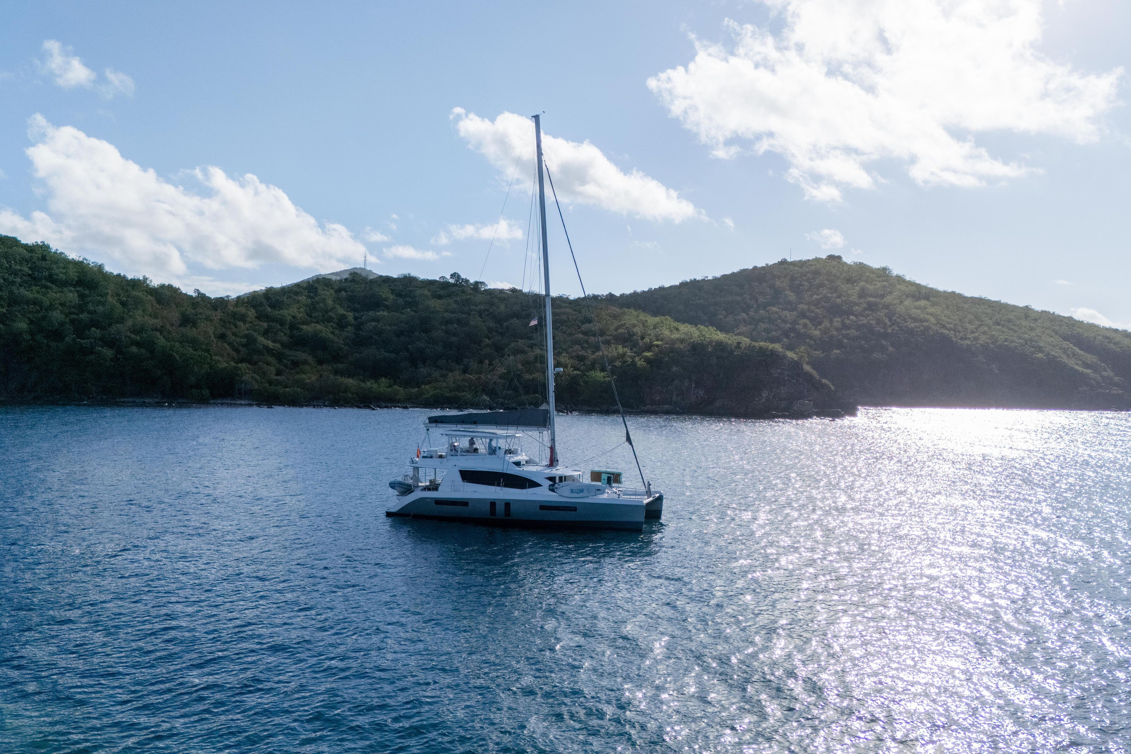 Sailing yacht Leopard 58, 2014 model, anchored in serene bay with lush hills.
