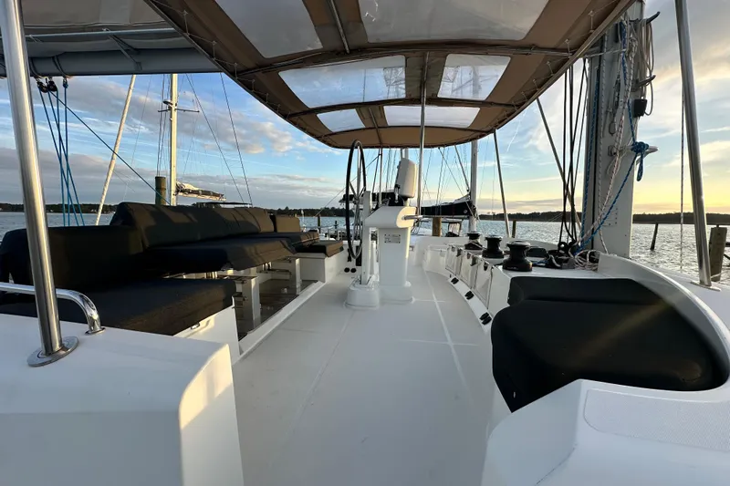 Rhapsody Yacht Photos Pics Lagoon 52 F 2021 catamaran deck with seating, under a canopy, at sunset on the water.