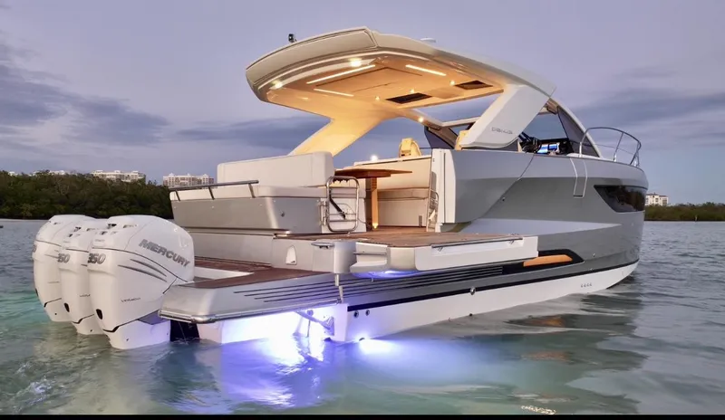  Yacht Photos Pics 2024 Jeanneau DB/43 OB yacht with illuminated deck and twin Mercury outboard engines at sunset.