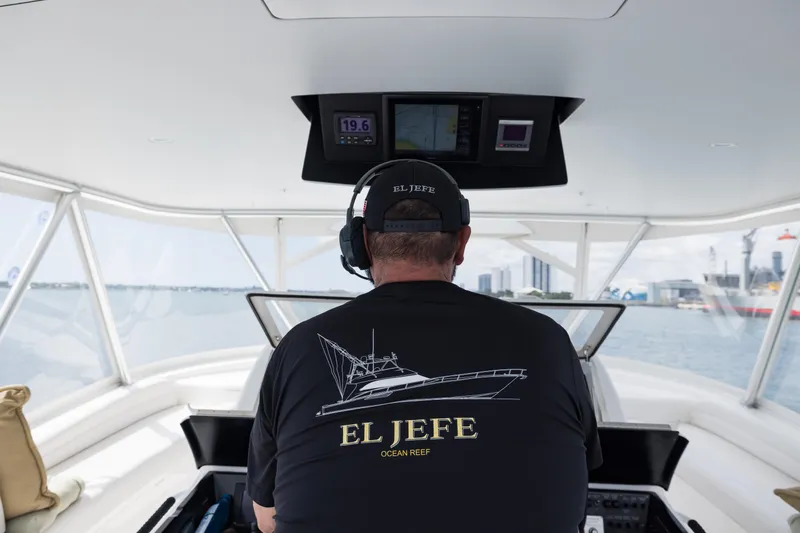 "el Jefe" Yacht Photos Pics Man steering 2014 Viking 70 Convertible yacht, wearing "El Jefe" shirt, with cityscape in background.