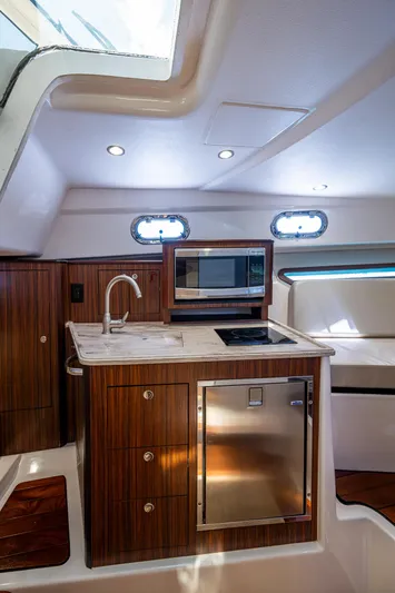 Cay Day Yacht Photos Pics 2017 Pursuit 325 OS yacht interior with kitchenette, featuring wood cabinetry, sink, and microwave.