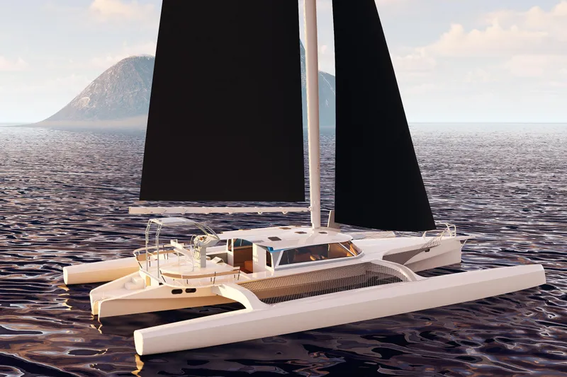  Yacht Photos Pics 2026 Rapido 63 trimaran sailing on calm ocean waters with distant island backdrop.
