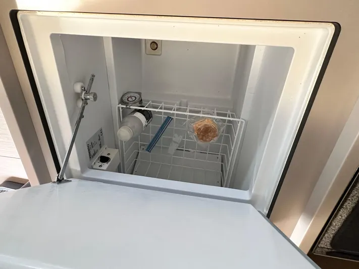 Chasing Summer Yacht Photos Pics Freezer compartment in 2022 Beneteau Oceanis 46.1 yacht, containing a wrapped item and a bottle.