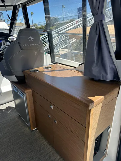 Destination Unknown II Yacht Photos Pics 2021 Jeanneau NC 895 interior with helm seat, wooden cabinetry, and window view.