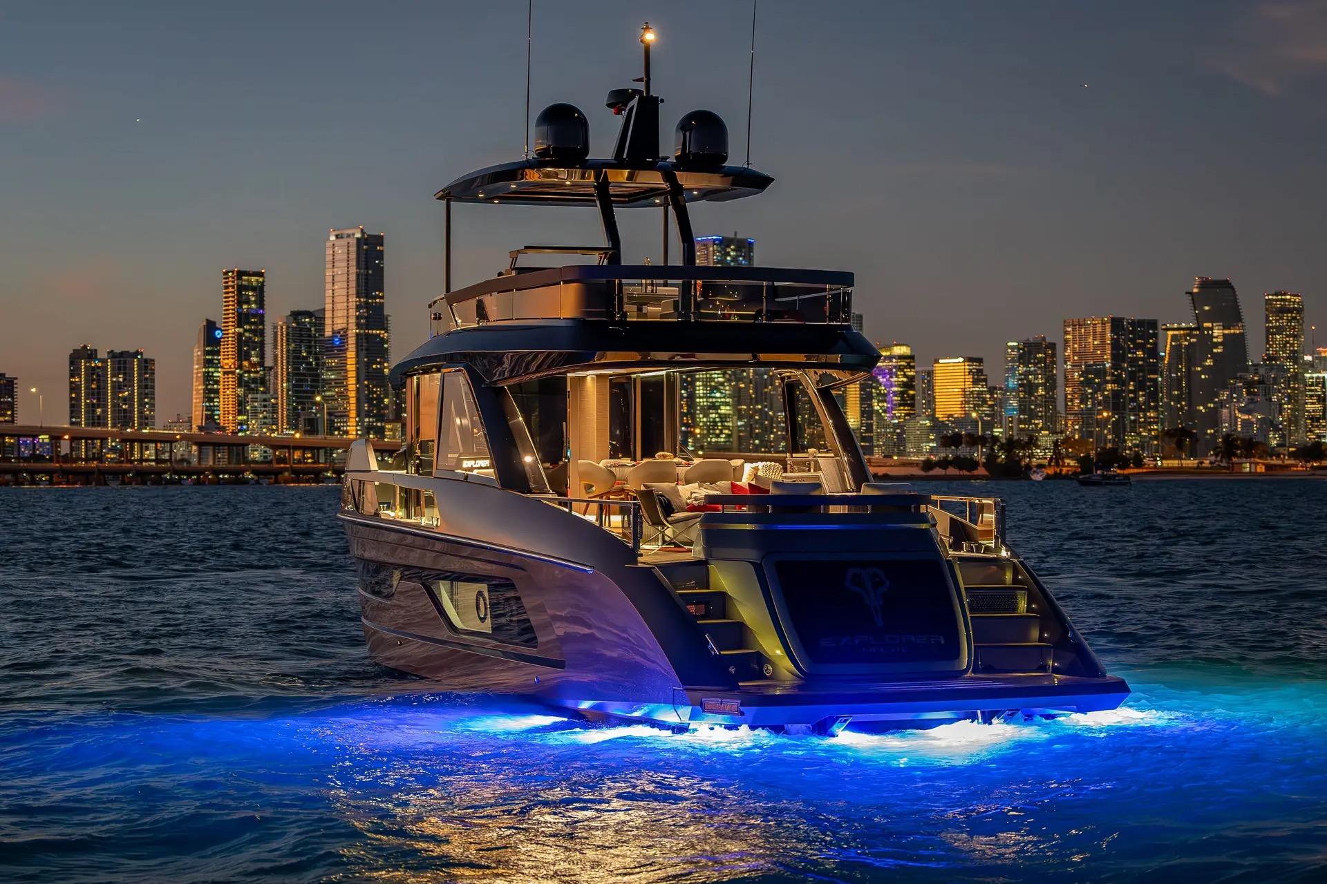 Luxurious 2025 Explorer 62 yacht illuminated against a vibrant city skyline at dusk.