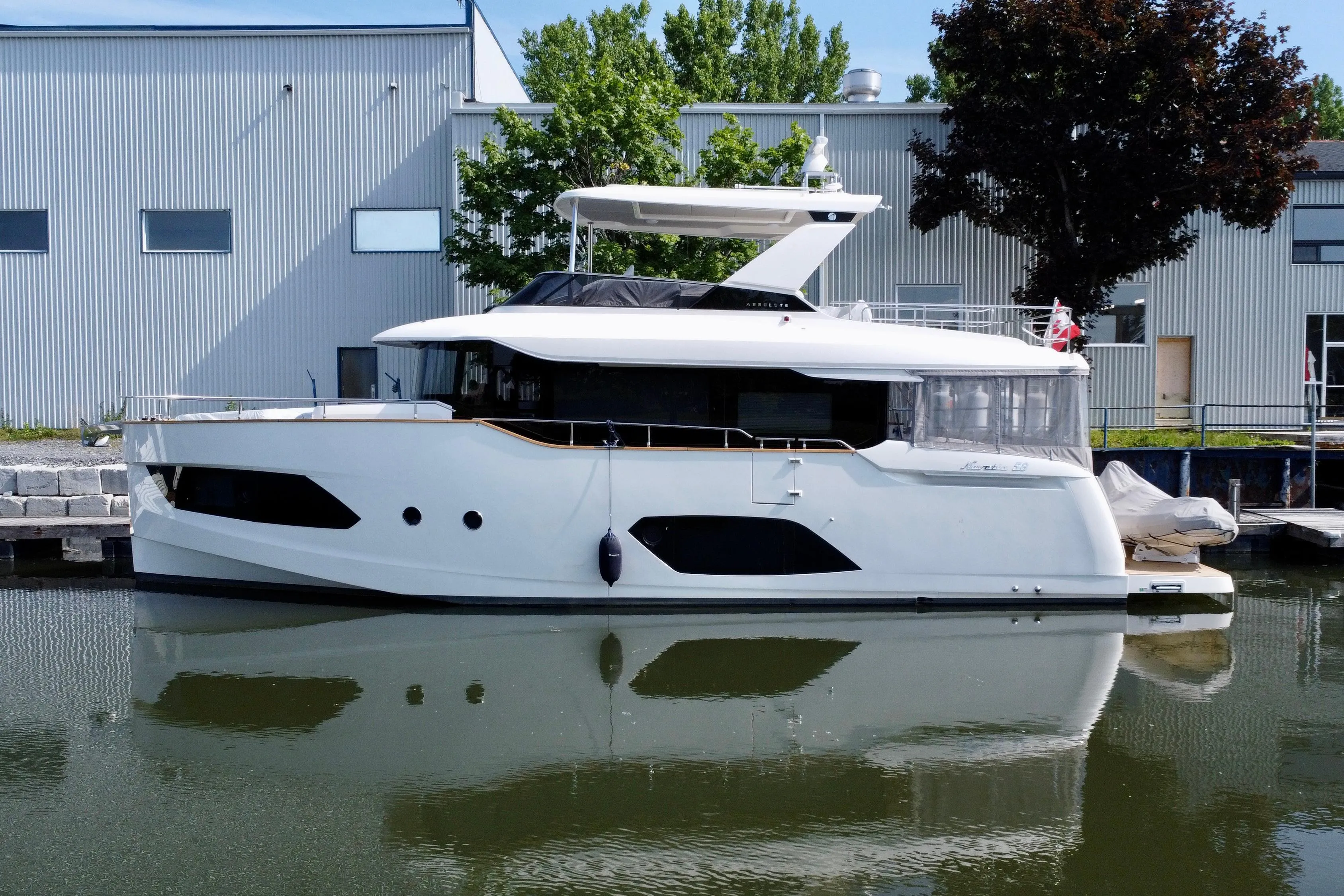 2024 Absolute 58 Navetta yacht docked by industrial buildings, reflecting on calm water.