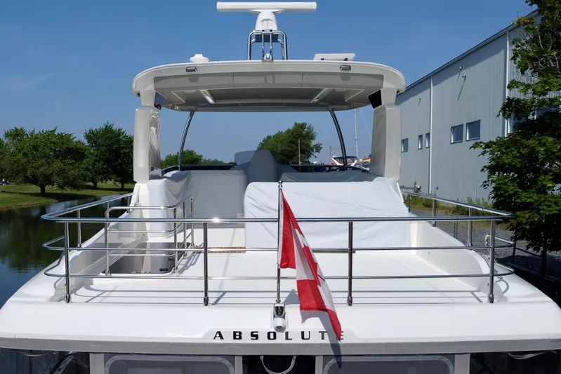  Yacht Photos Pics 2024 Absolute 58 Navetta yacht with spacious deck and red flag, docked near a building.