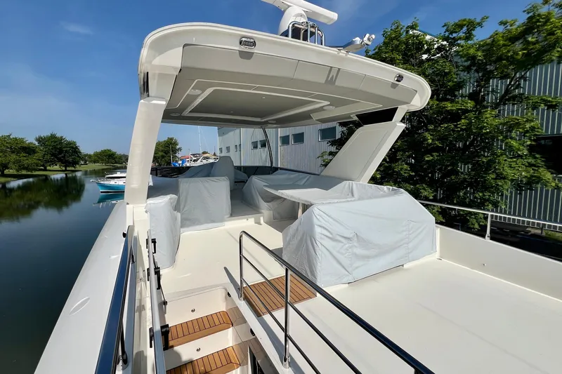  Yacht Photos Pics 2024 Absolute 58 Navetta yacht deck with covered seating, docked by calm water.
