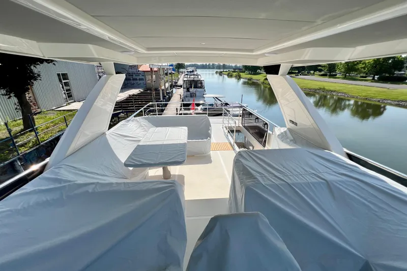  Yacht Photos Pics 2024 Absolute 58 Navetta yacht deck with covered seating, docked by a serene waterway.