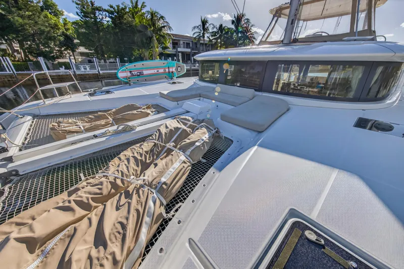 White Heron Yacht Photos Pics 2021 Lagoon 46 Owner's Version catamaran with sunbathing area and paddleboard, docked in a tropical setting.