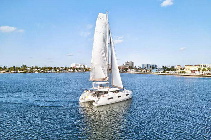 White Heron Yacht Photos Pics 2021 Lagoon 46 Owner's Version catamaran sailing in a sunny coastal harbor.