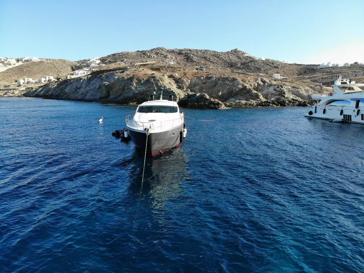  Yacht Photos Pics 2007 Pershing 62 yacht anchored in clear blue waters near rocky coastline.