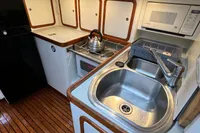Compact kitchen in a 1999 Custom Tasman 48 yacht with sink, stove, and microwave.