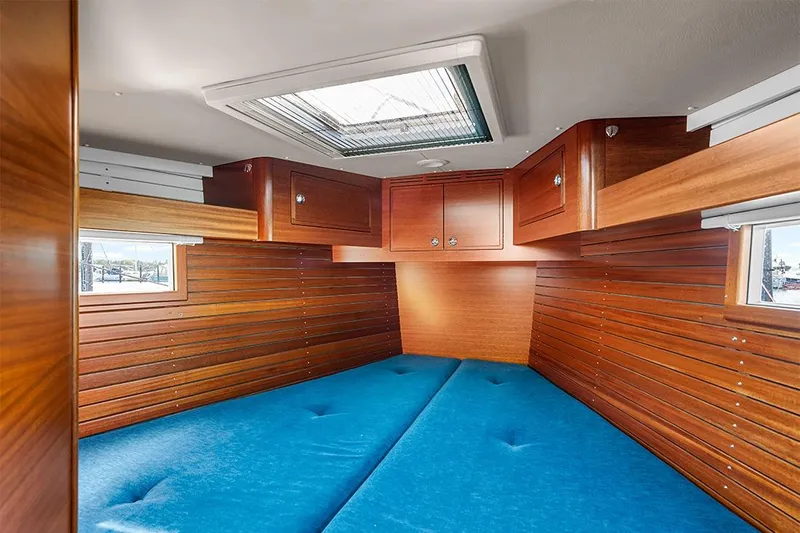  Yacht Photos Pics Interior cabin of 2022 Hallberg-Rassy 400 yacht with wooden paneling and blue cushions.
