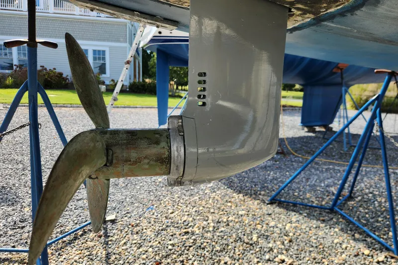 Glendora Yacht Photos Pics Close-up of a 2007 Hallberg-Rassy 37 sailboat propeller and rudder on a gravel surface.