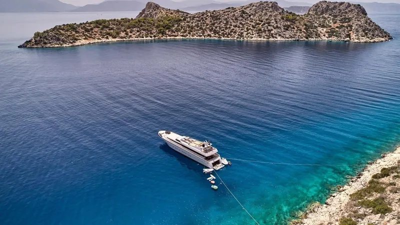 Kintaro Yacht Photos Pics Luxury yacht Cantieri di Pisa Akhir 38, 2005, anchored in serene turquoise waters near a rocky island.