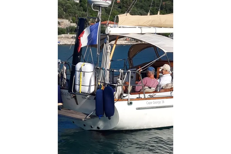 Begonia Yacht Photos Pics Sailboat "Cape George 38" with passengers, featuring French flag, docked in scenic harbor.