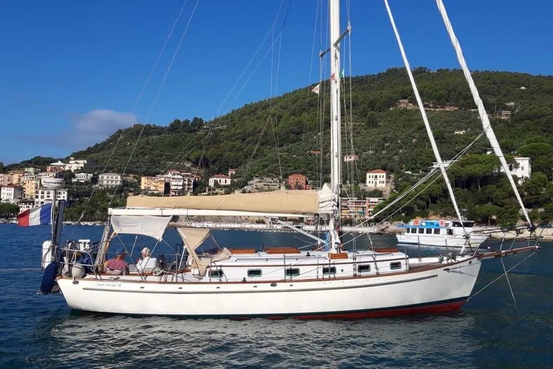 Begonia Yacht Photos Pics Sailboat "Atkin & Lange Cutter" 1988 on scenic coastal waters with hillside town backdrop.