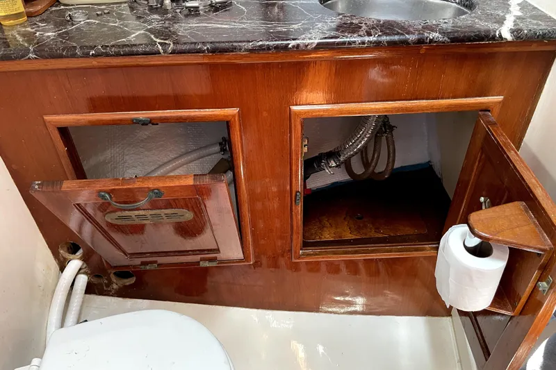 Begonia Yacht Photos Pics Wooden cabinet with open doors, plumbing pipes, and a marble countertop in a 1988 Atkin & Lange Cutter.