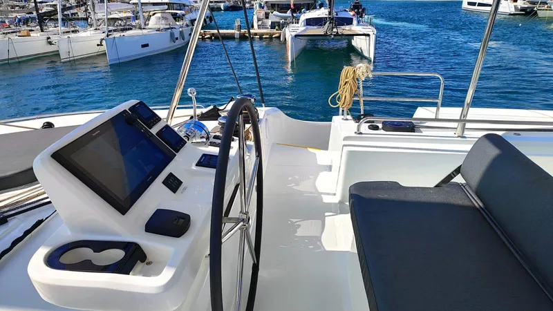  Yacht Photos Pics 2024 Lagoon 51 yacht cockpit with steering wheel and navigation screens, docked in a marina.