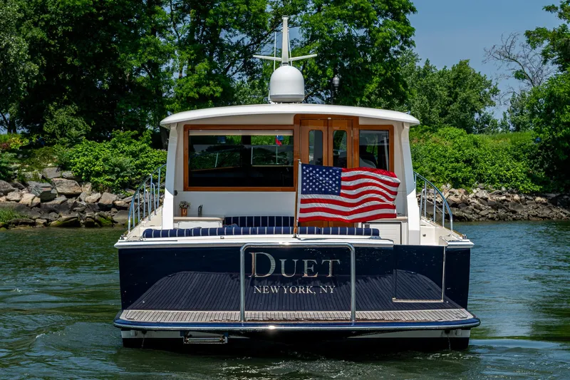 Duet Yacht Photos Pics 2017 Grand Banks 44 Eastbay SX yacht with American flag, cruising near lush greenery.