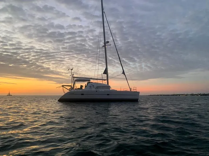 Tortuga Yacht Photos Pics Lagoon 380 catamaran sailing at sunset, 2001 model, silhouetted against a colorful sky.